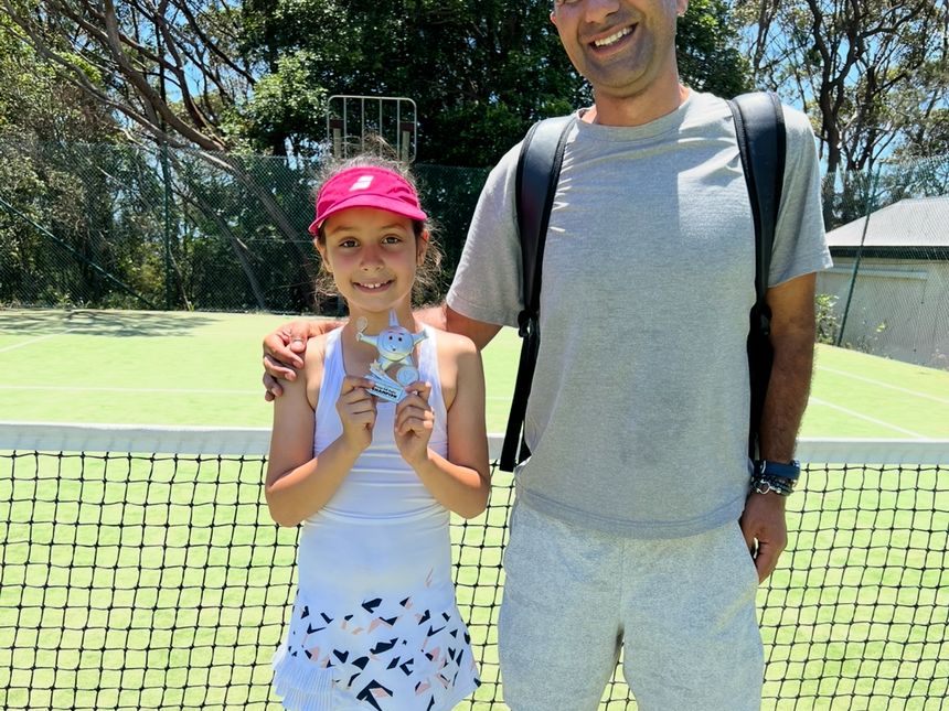 A junior player with their trophy at the net
